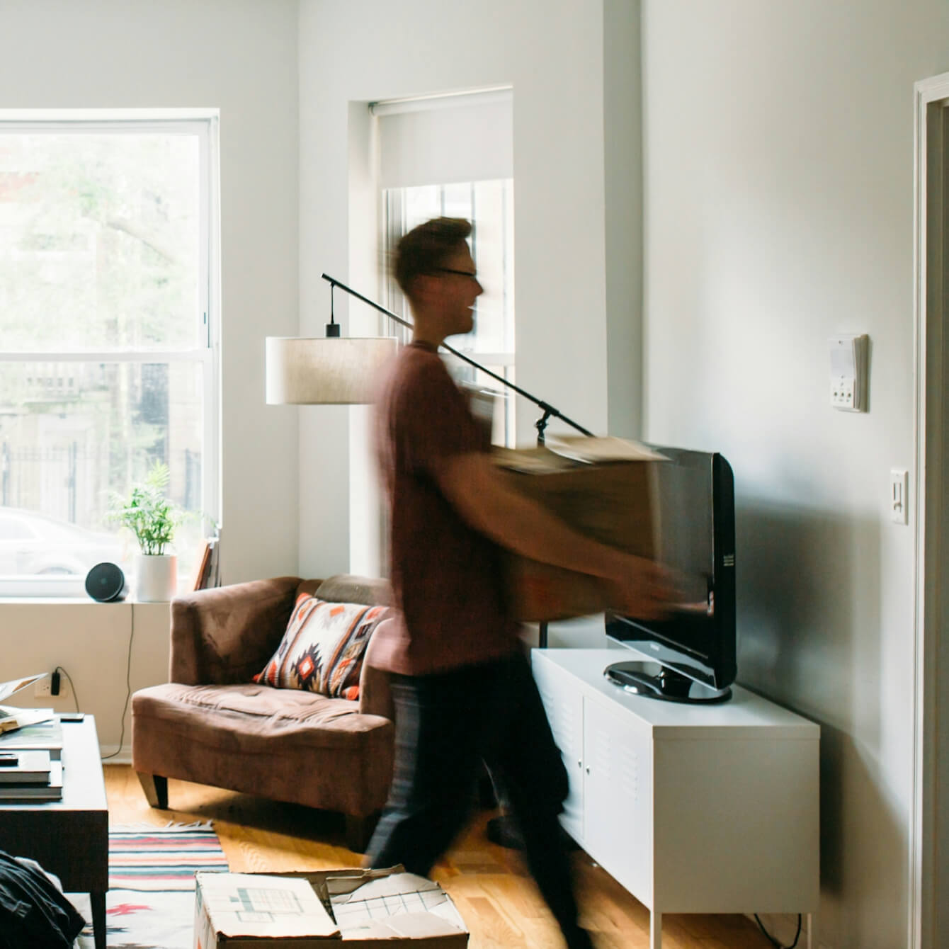 A person carrying a moving box through a living room while packing up