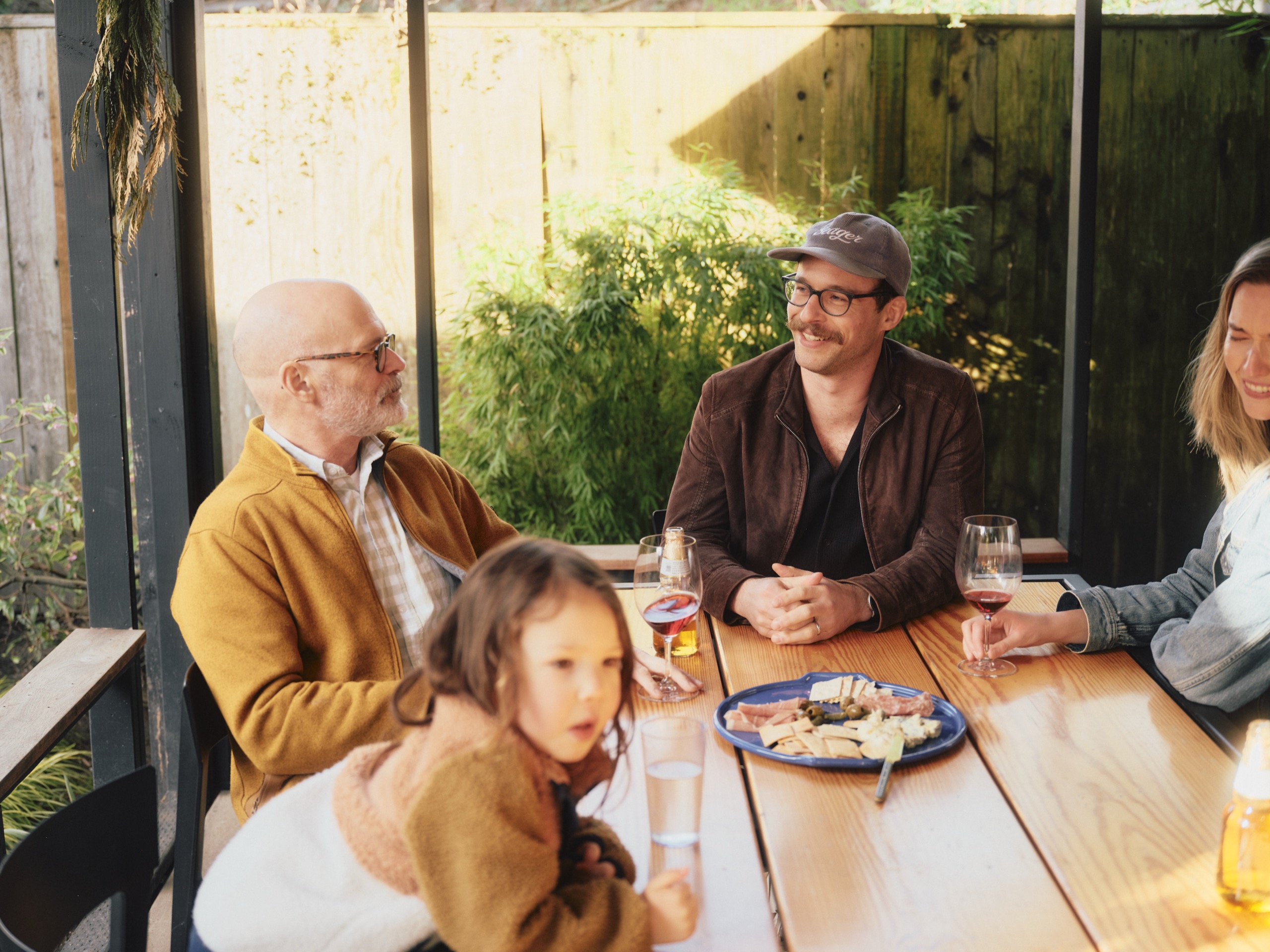 Three generations of a family sharing wine and a charcuterie board at an outdoor table